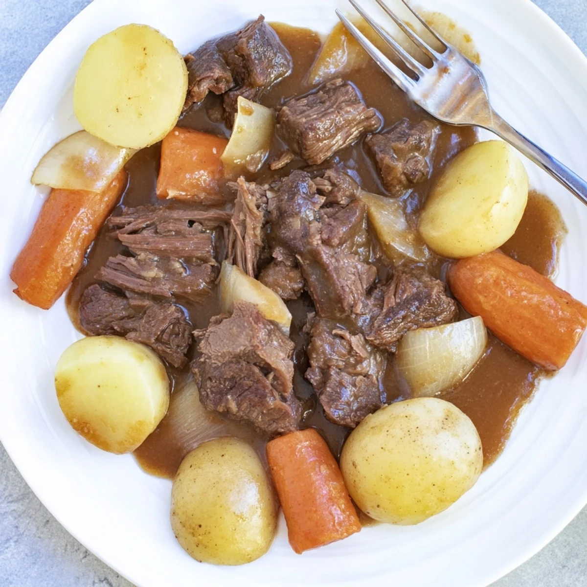 Golden-brown pot roast in slow cooker, garnished with fresh thyme, surrounded by tender carrots and potatoes in rich savory gravy.  