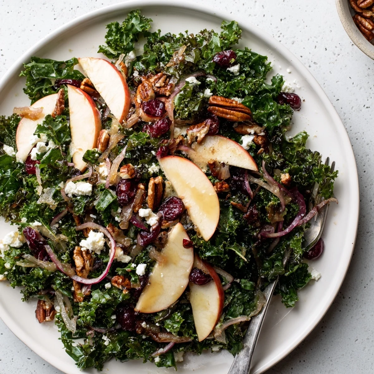 Freshly toasted pecans and ruby-red cranberries scattered over vibrant green kale in a bowl of Winter Kale Salad.