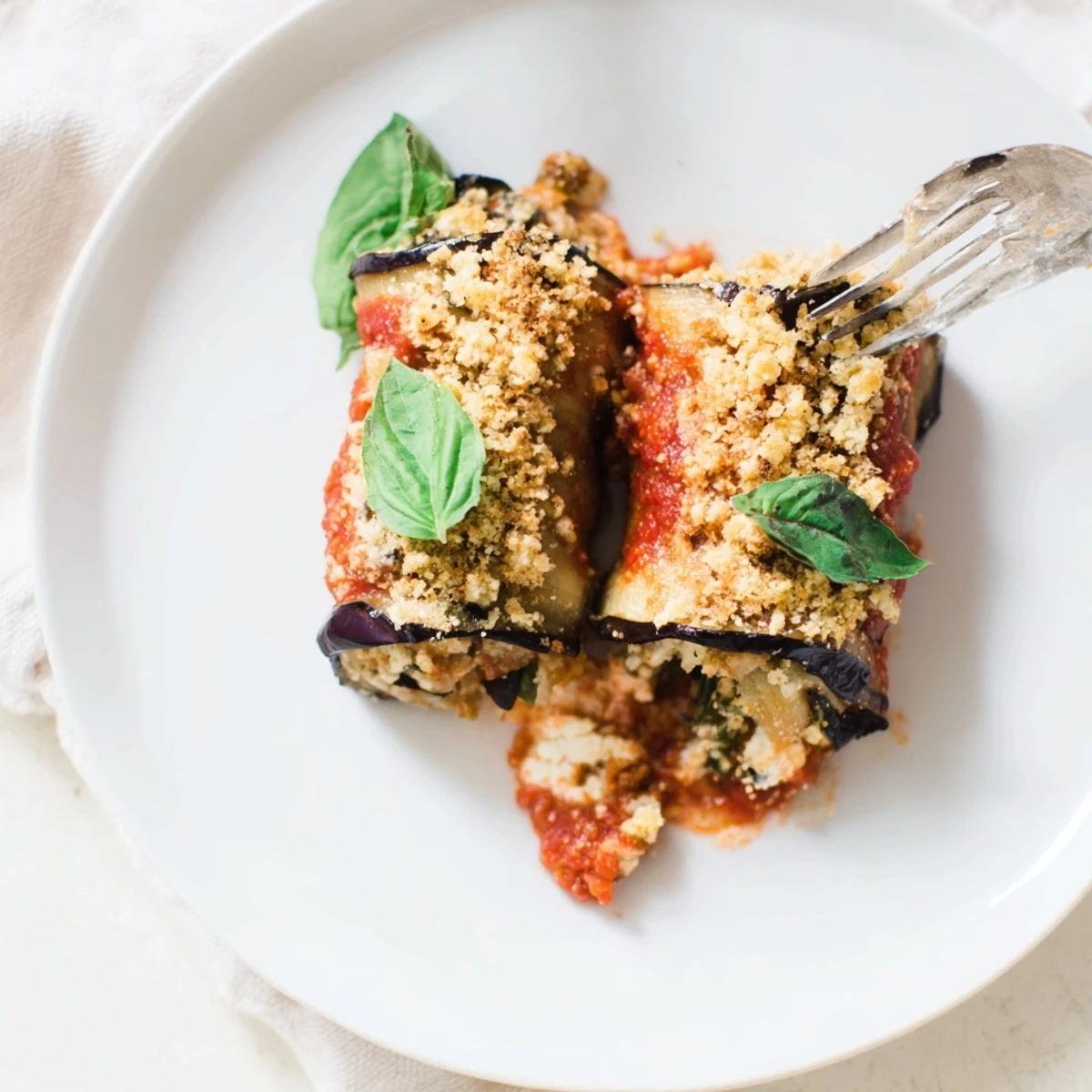 A close-up of cheesy baked eggplant rollatini, bubbling with marinara and topped with fresh basil garnish.
