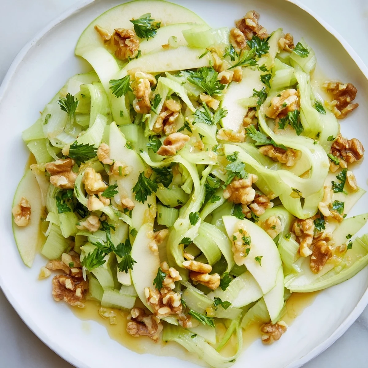 A close-up of a serving bowl of Green Apple and Celery Salad with Walnuts, glistening with a light vinaigrette and fresh parsley garnish.
