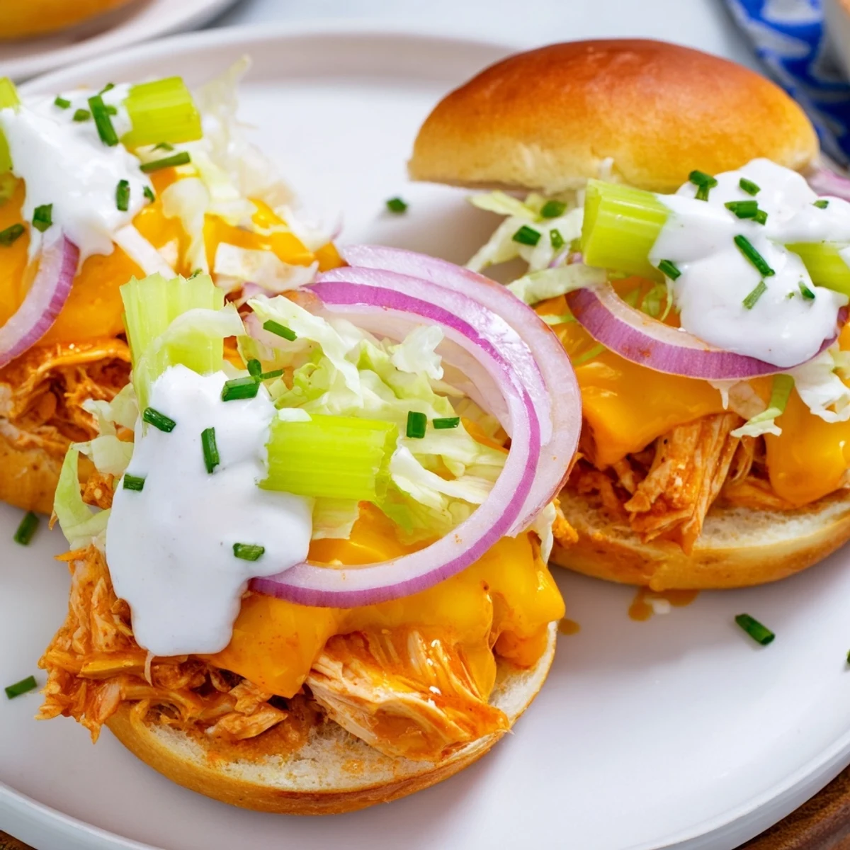 Freshly baked Buffalo Chicken Sliders with Ranch Dressing topped with melted cheddar and celery, ready to be enjoyed warm.