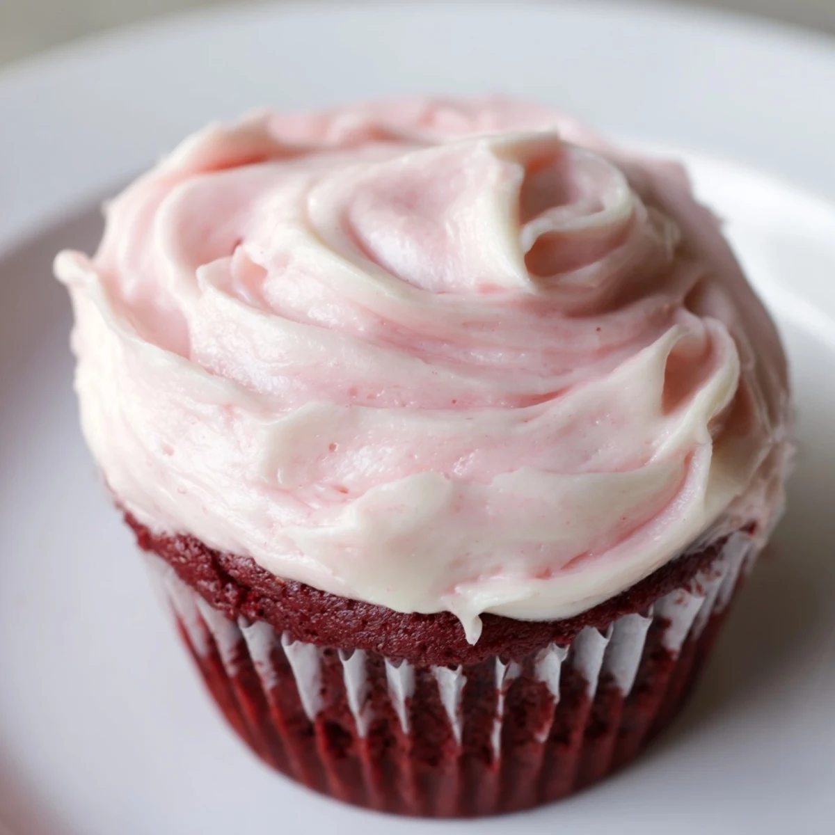 Freshly baked Red Velvet Cupcakes with Pink Cream Cheese Frosting, showcasing moist red crumb and swirls of pastel frosting on a marble board.