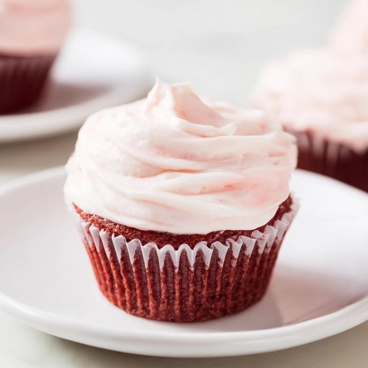 Close-up of a Red Velvet Cupcake with Pink Cream Cheese Frosting, revealing its velvety texture as the piped swirl is lifted by a spatula.