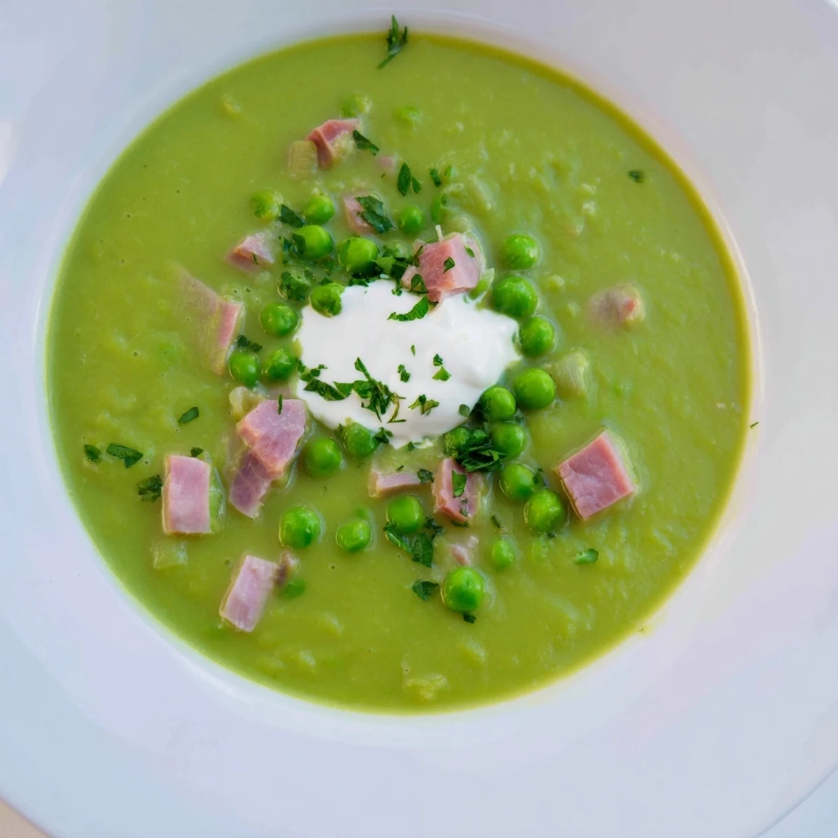 A close-up of Spring Pea Soup with Ham and Turkey, featuring tender peas and savory chunks of meat in a creamy broth, garnished with fresh parsley.  