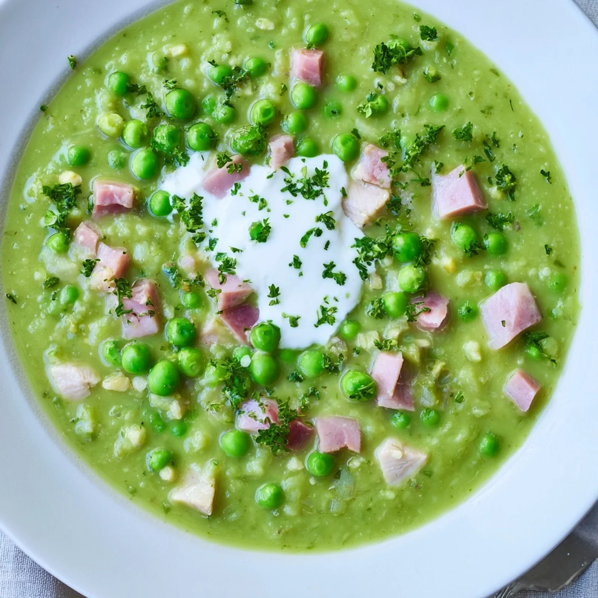 Vibrant green Spring Pea Soup with Ham and Turkey served hot in a rustic bowl, with a dollop of crème fraîche and crusty bread on the side.  