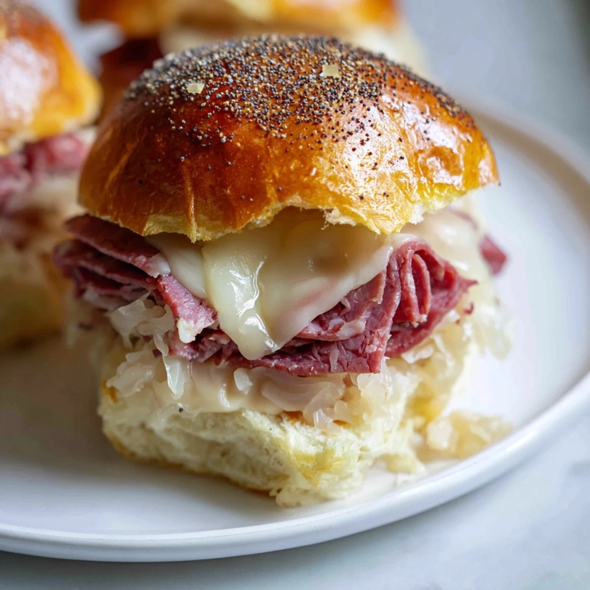 A close-up of warm Corned Beef Sliders with Swiss cheese, melted and bubbling on soft Hawaiian rolls with a tangy sauce.