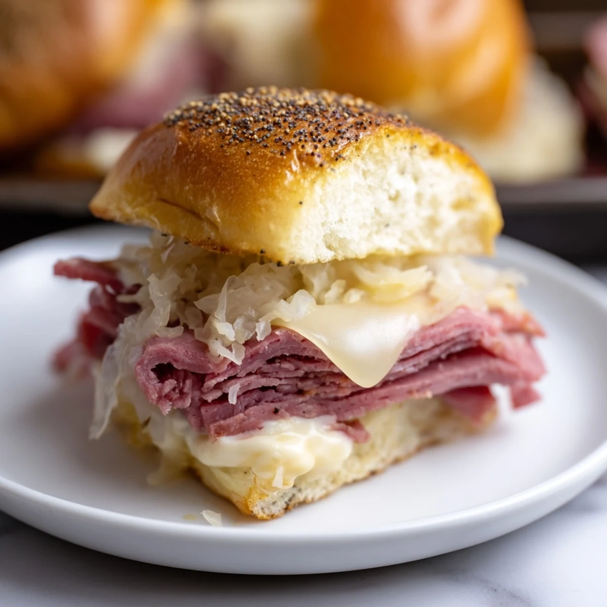 A baking sheet of freshly baked Corned Beef Sliders with Swiss cheese, golden poppy seed tops, and a side of pickles.