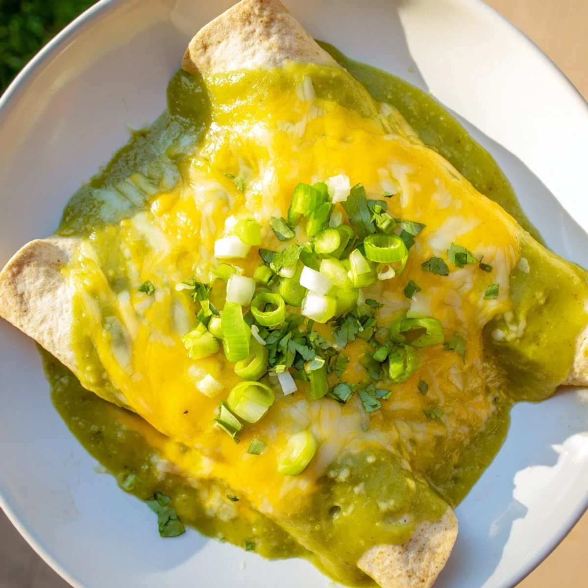 Close-up of Beef Enchiladas with Green Chili Sauce featuring melted cheese, sour cream, and chopped onions.