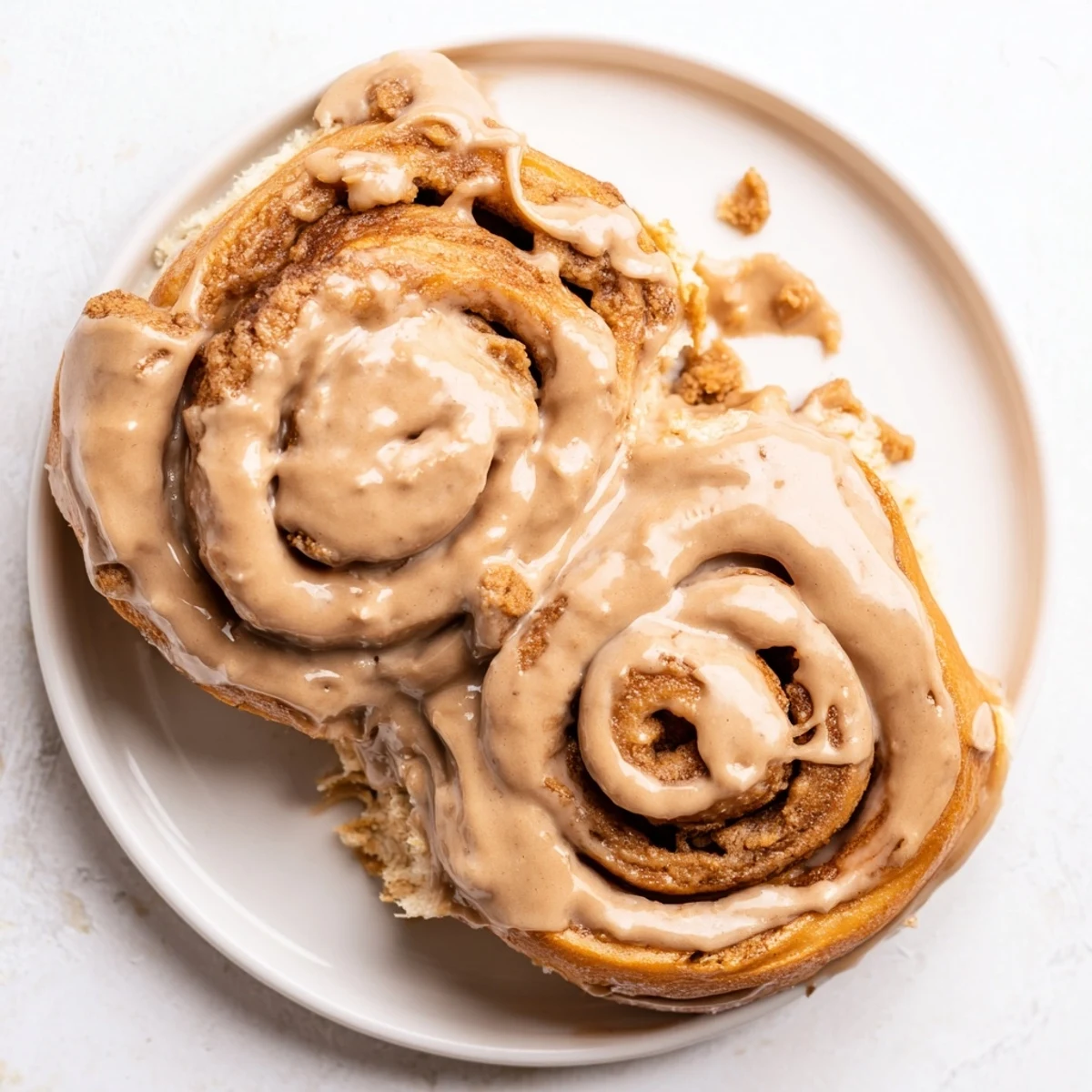 Freshly baked Soft and Gooey Biscoff Cinnamon Rolls sit in a ceramic dish, swirled with brown sugar and dripping with warm glaze.  