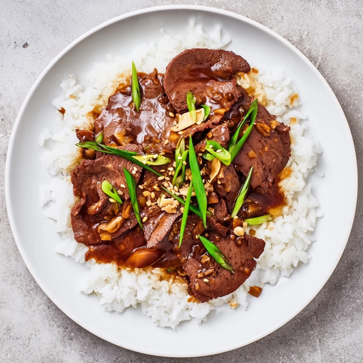 Slow cooker Mongolian beef features tender beef strips in a glossy, savory-sweet sauce over fluffy white rice with green onions.