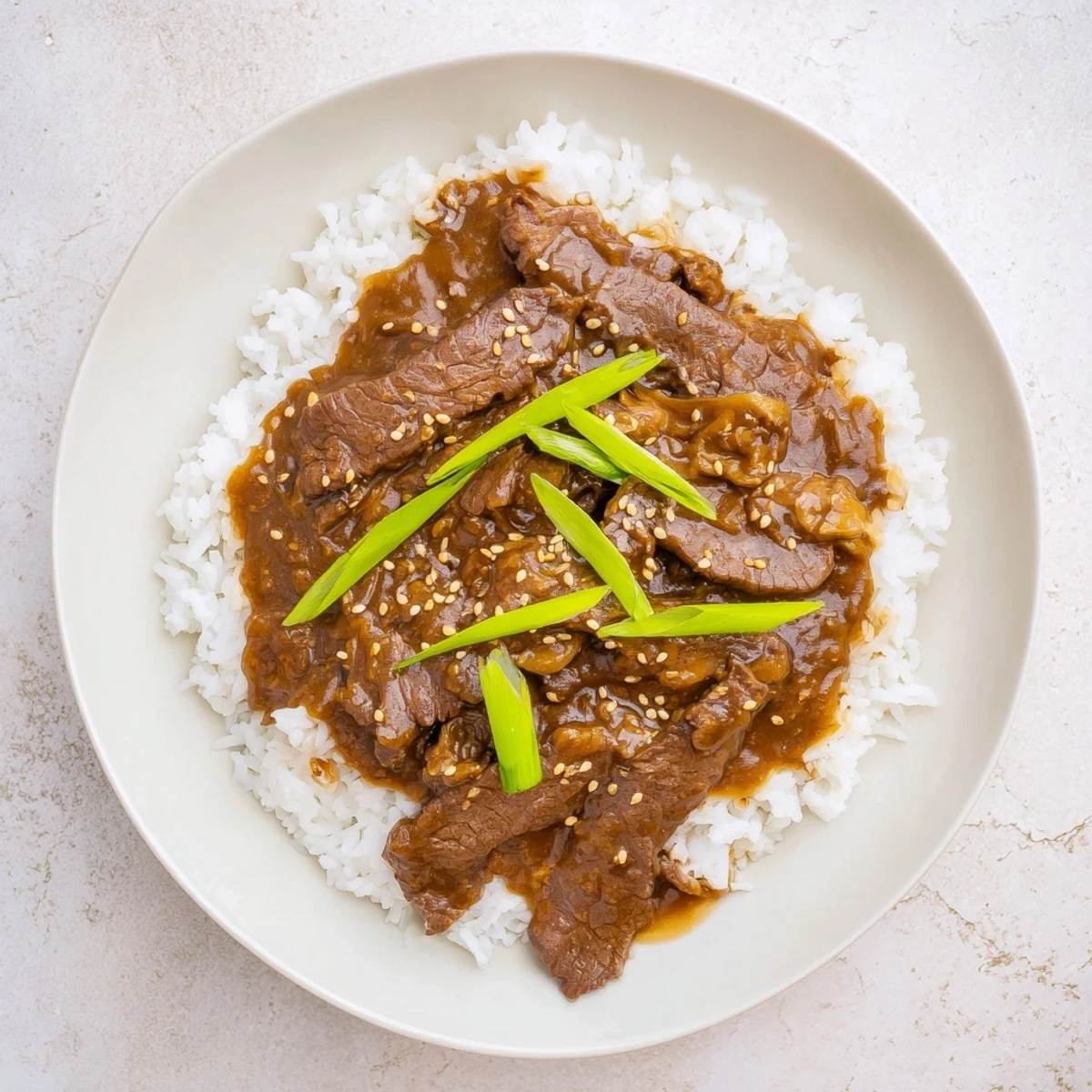A close-up of Ultimate Slow Cooker Mongolian Beef, saucy beef morsels glistening with garlic and ginger, ready to eat.