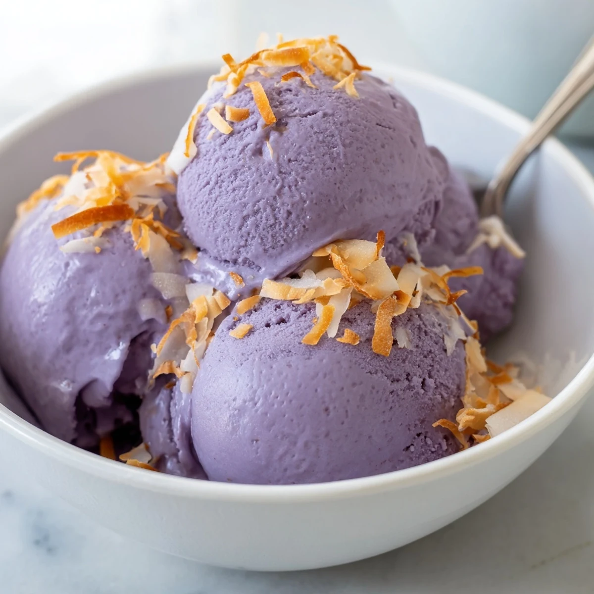 A scoop of ube ice cream melts slightly beside ube halaya, highlighting its sweet, velvety texture.