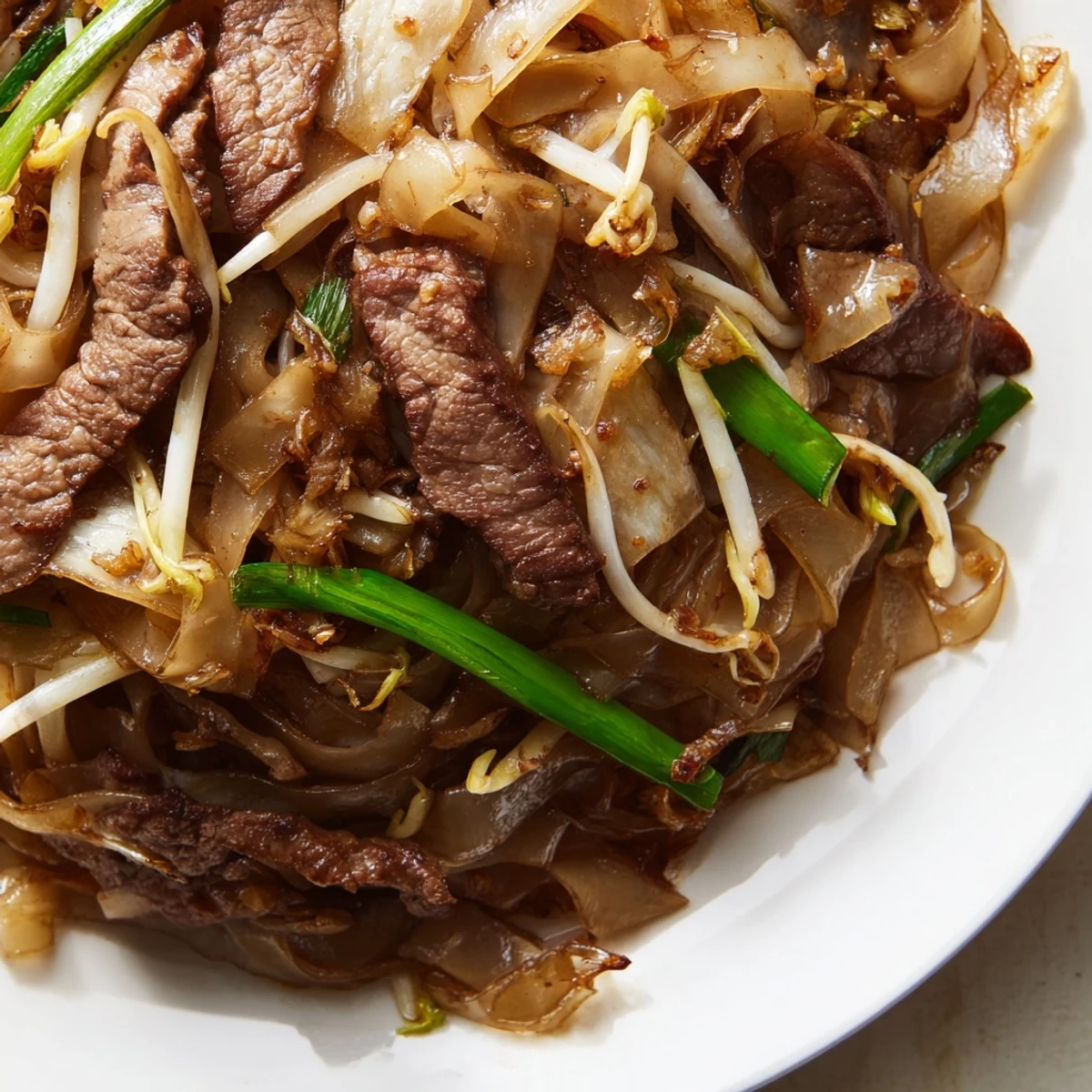 Golden-brown seared beef and wide rice noodles in a glossy savory sauce, with crisp bean sprouts and green onions in Beef Chow Fun.