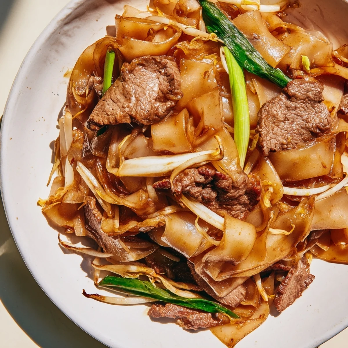 A close-up of sizzling Beef Chow Fun showing tender beef strips, wide noodles, and fresh bean sprouts, ready to serve hot.