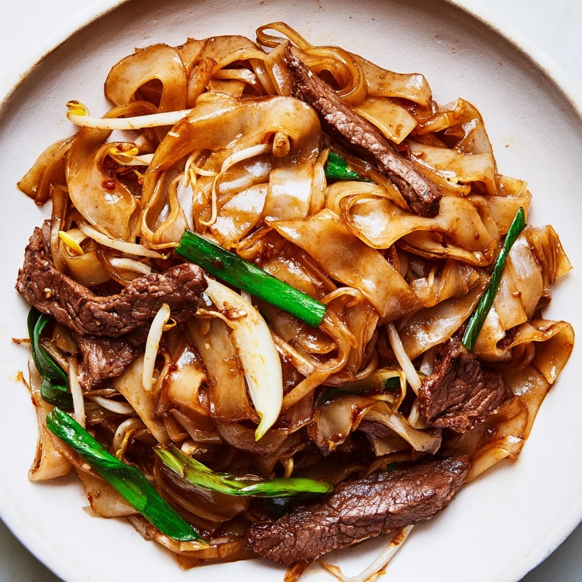 Hearty homemade Beef Chow Fun with charred wide noodles, beef, and vegetables, plated for a delicious Chinese weeknight dinner.
