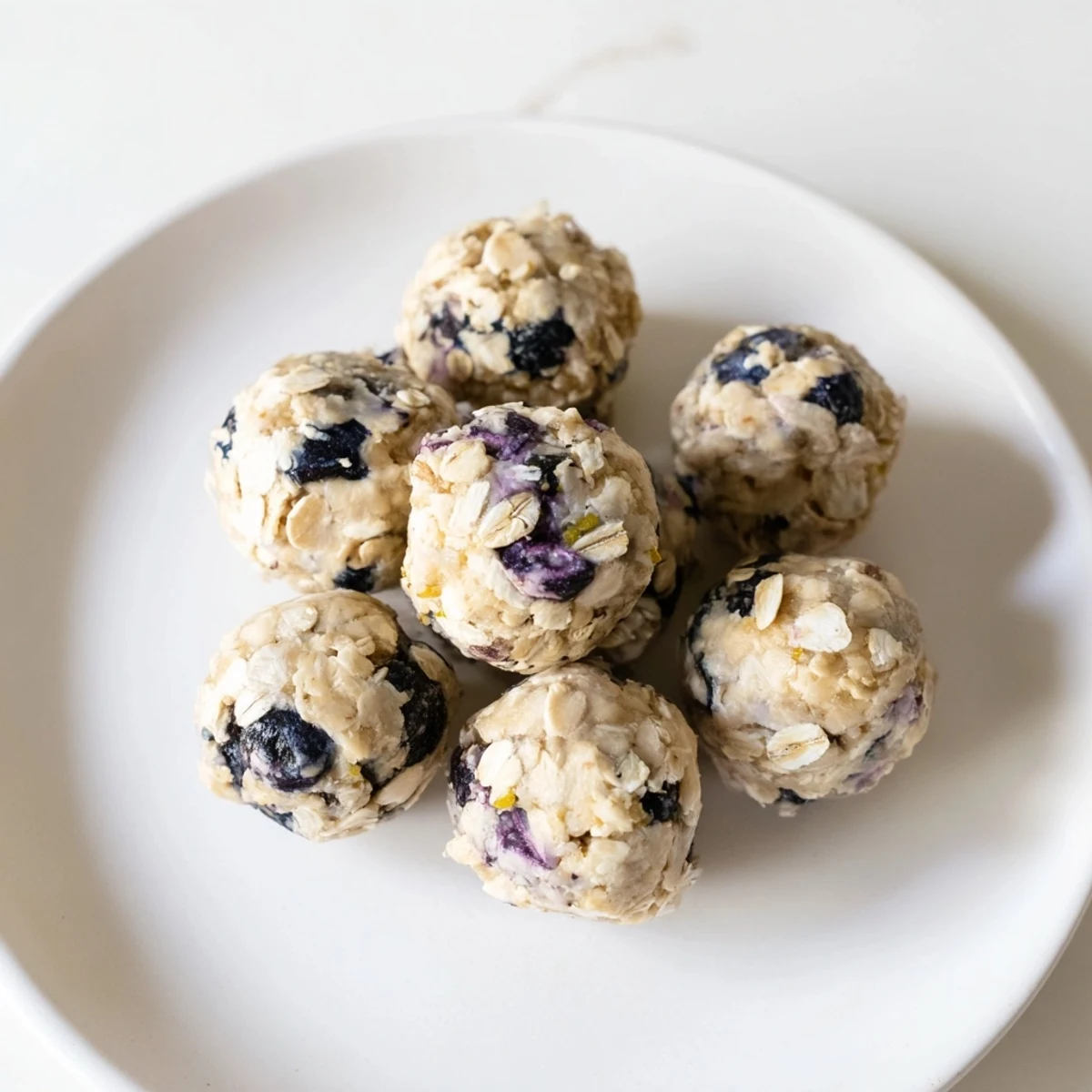 Twelve rolled-oat protein bites with fresh blueberries and cream cheese on a wooden board.