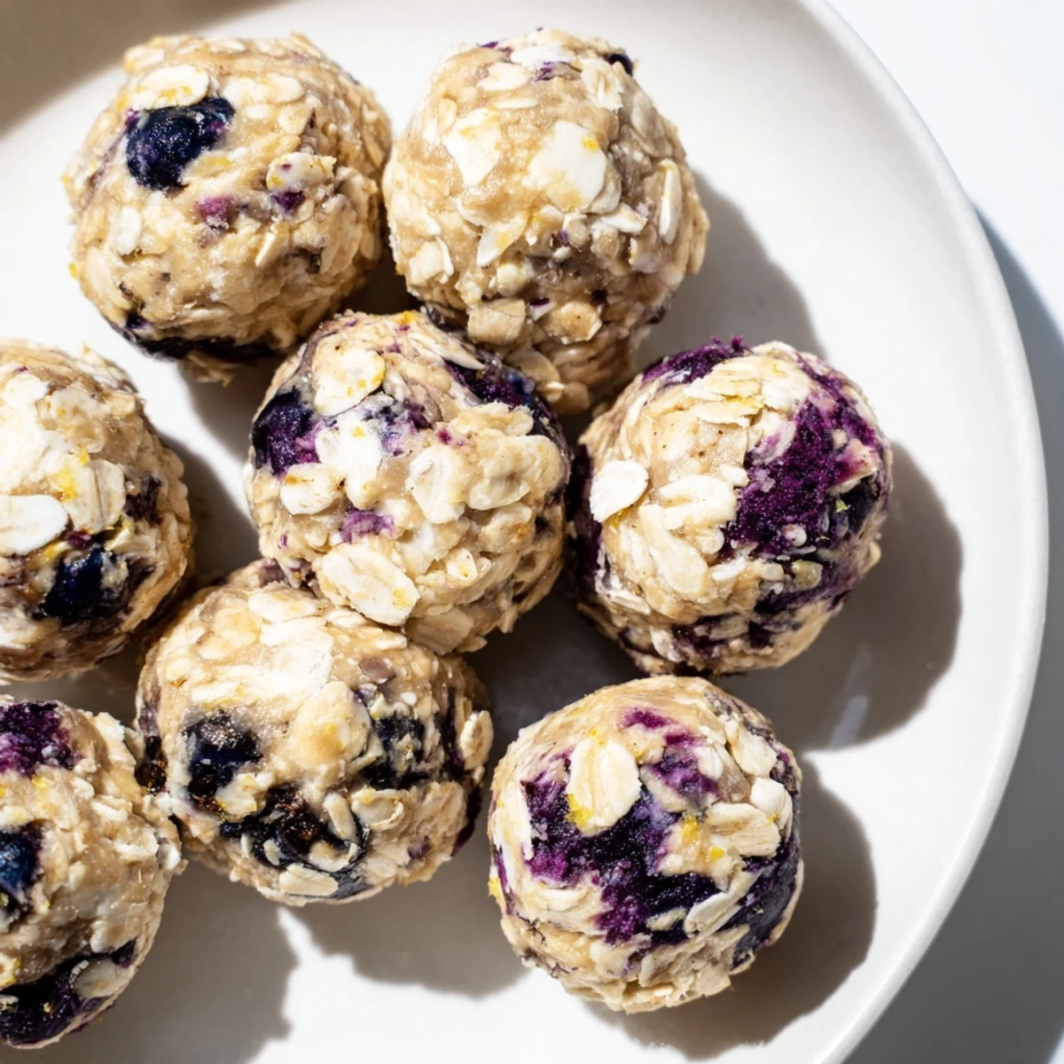 Gluten-free, no-bake Blueberry Cheesecake Protein Bites stacked on a parchment-lined tray.