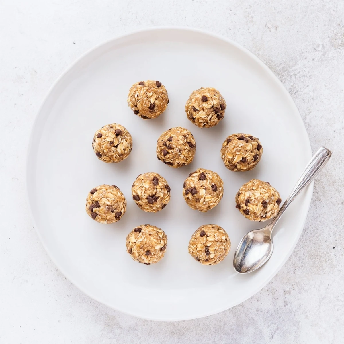 Twelve mint chocolate chip protein balls on a white plate, showing their chewy texture and glistening chocolate chips.