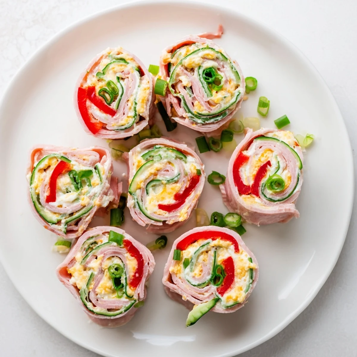 Fresh keto ham roll ups arranged on serving platter with cucumber and green onion garnish