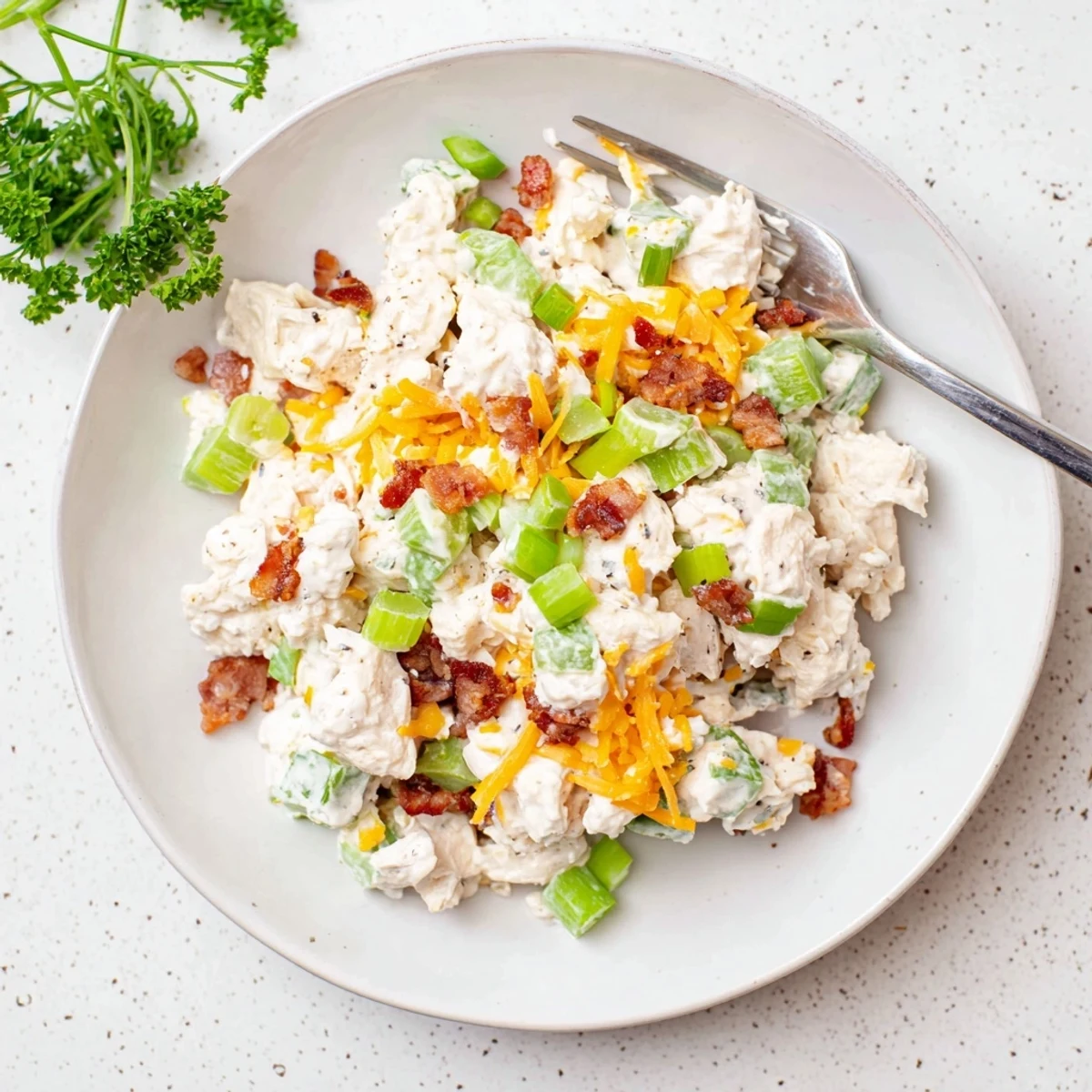 Creamy low carb jalapeno popper cottage cheese chicken salad topped with crispy bacon crumbles and fresh diced jalapeños in a white serving bowl