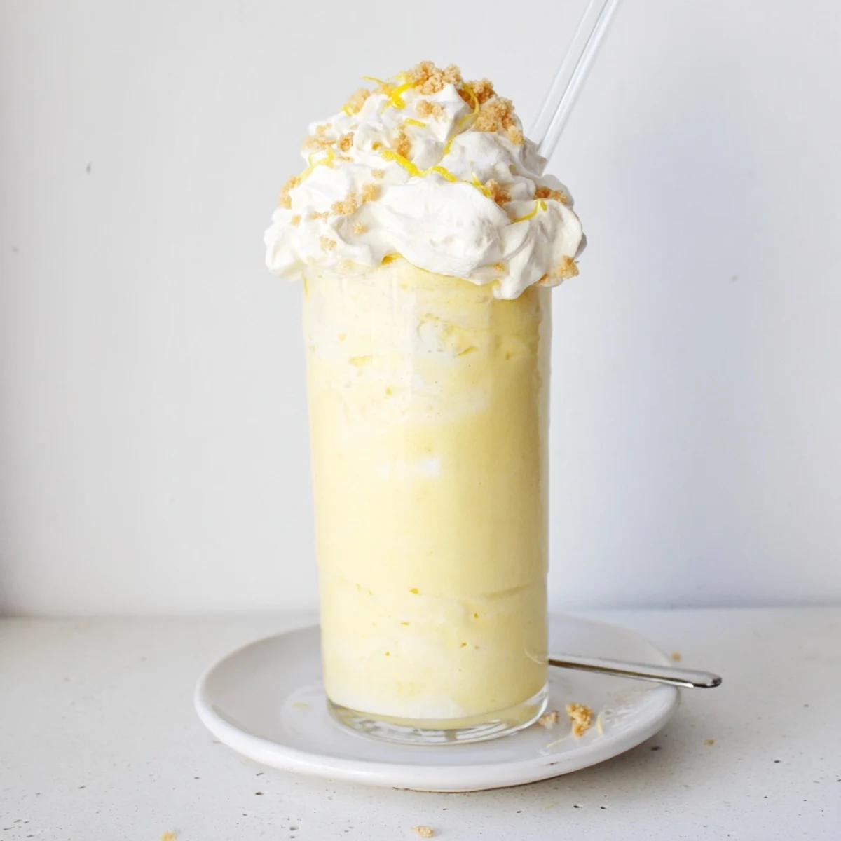 Tall glass of lemon meringue frappé topped with fluffy white meringue and lemon zest garnish