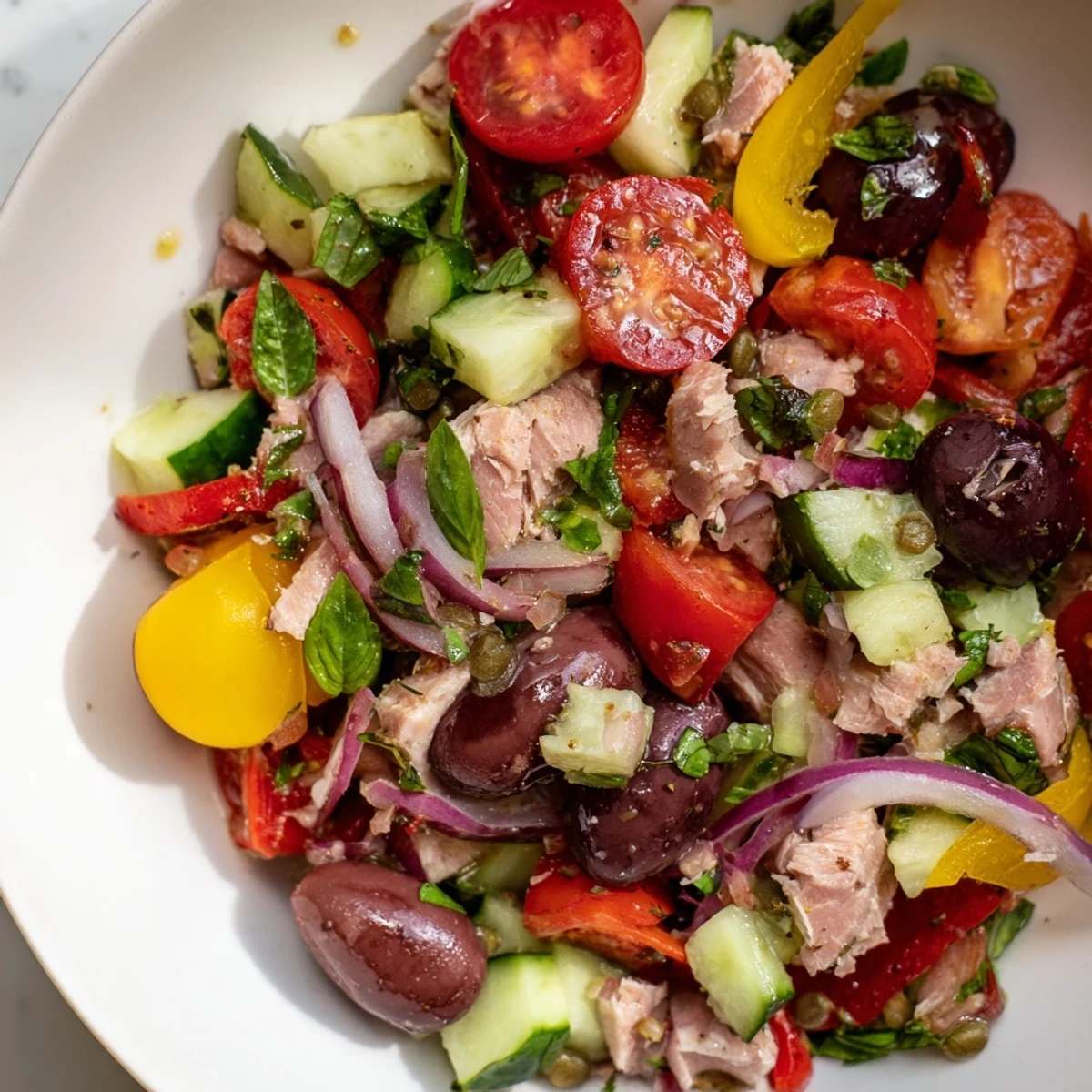 Healthy Mediterranean tuna salad featuring cherry tomatoes, cucumbers, Kalamata olives, and bright herbs