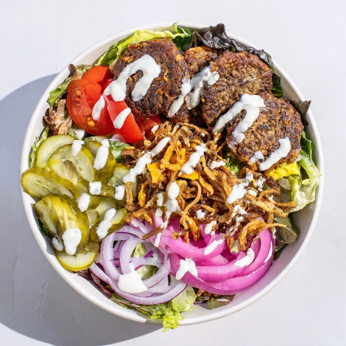 Golden crispy smash burger patties nestled over fresh salad greens with juicy tomatoes and creamy drizzle