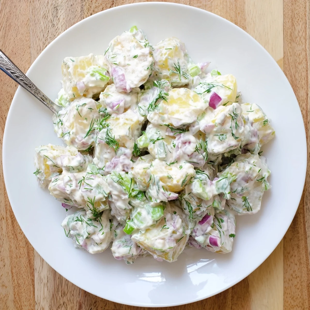Creamy Greek yogurt potato salad with tender potatoes, red onion, celery, and fresh green herbs.
