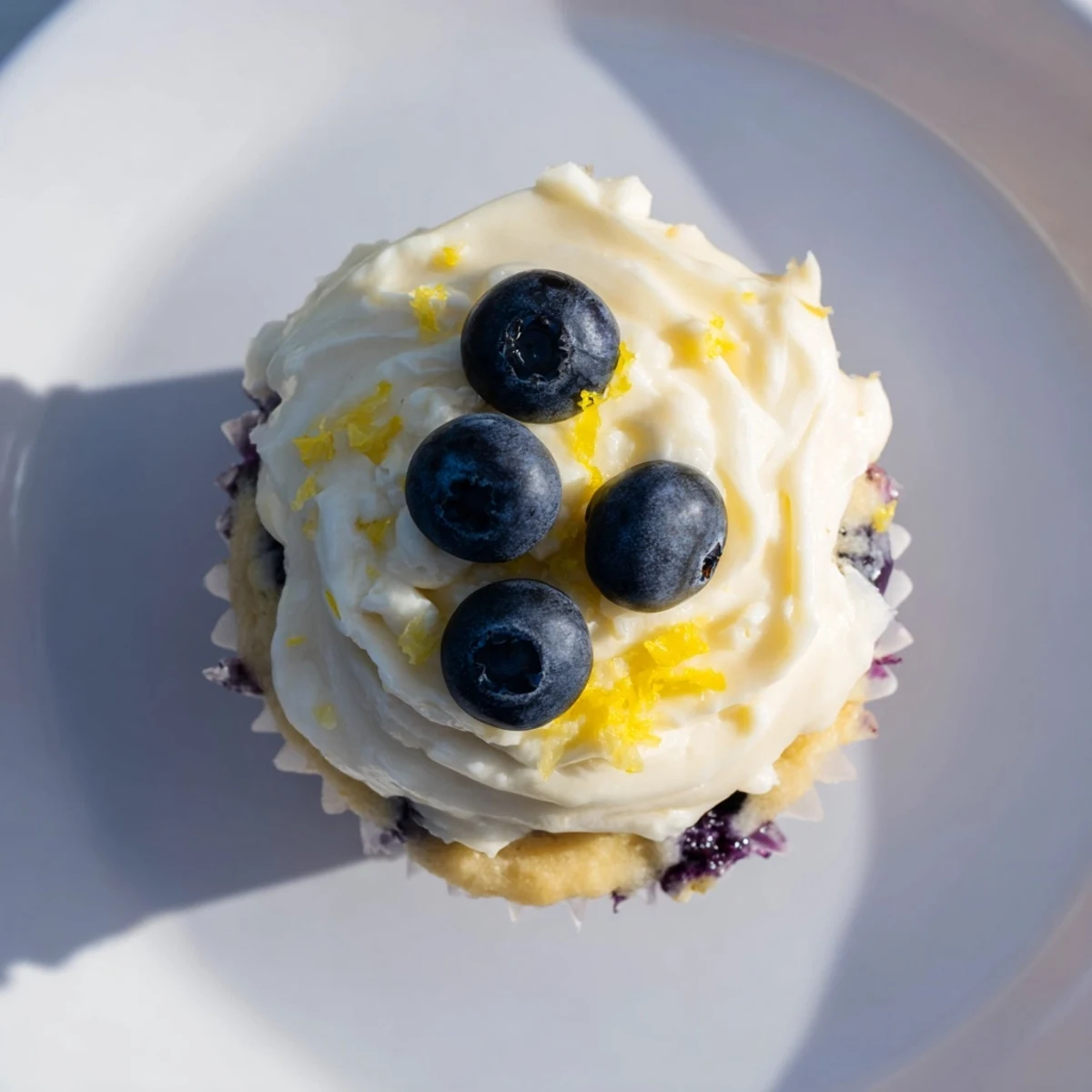 Golden lemon blueberry cupcakes topped with swirls of tangy cream cheese frosting and fresh blueberries