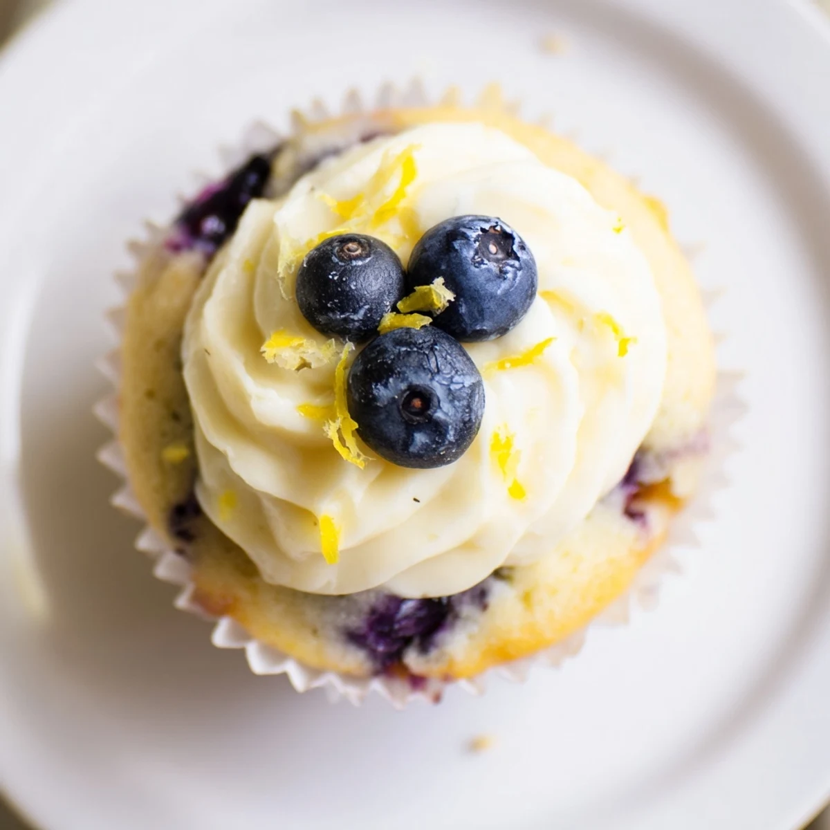 Freshly baked lemon blueberry cupcakes with citrus cream cheese frosting garnished with lemon zest and whole berries