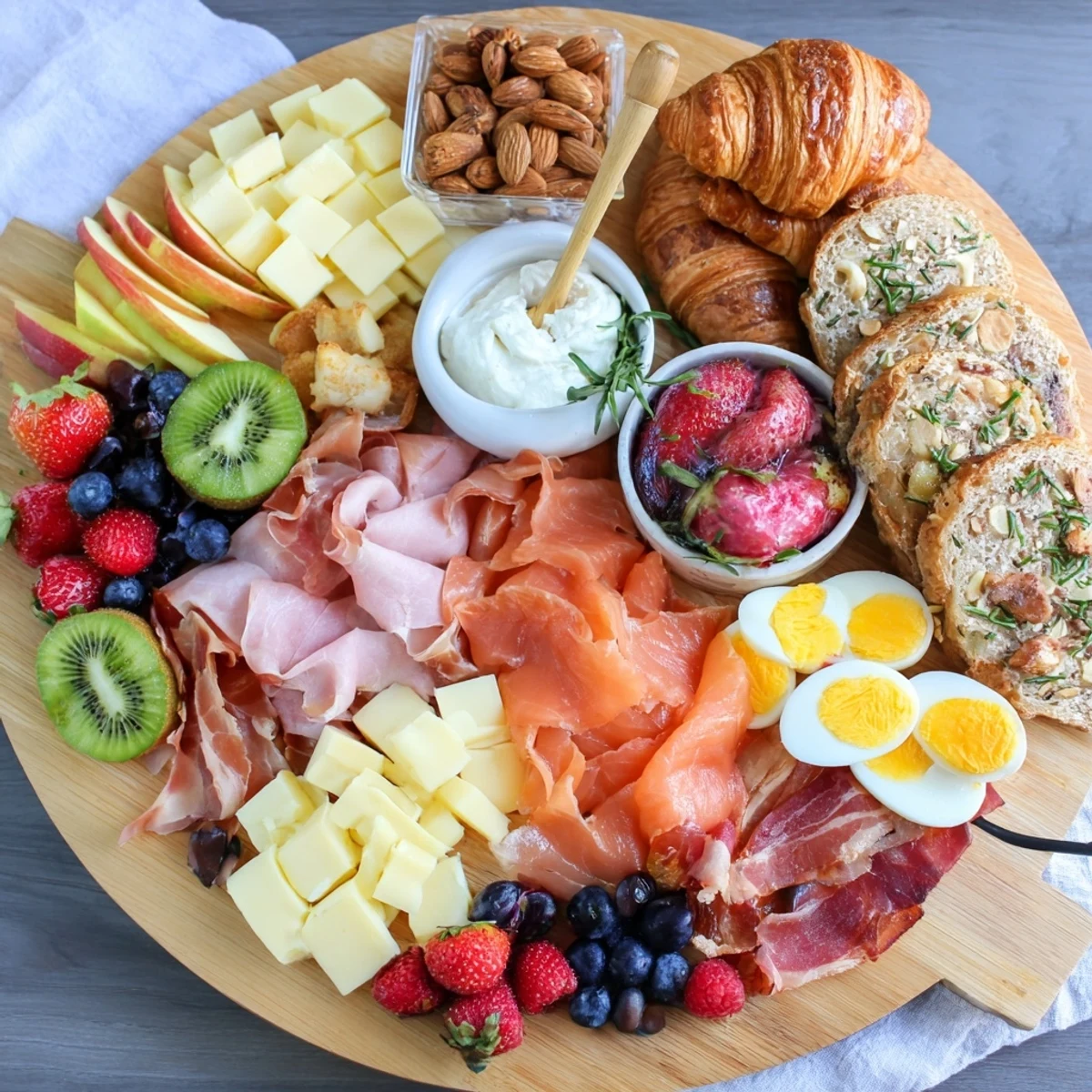 Wooden breakfast charcuterie board with prosciutto, brie, berries, and croissants arranged for sharing