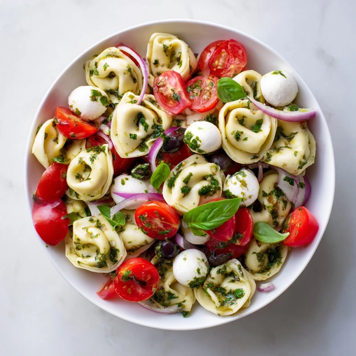 Cheese tortellini pasta salad tossed with crisp vegetables and mozzarella in a rustic white dish