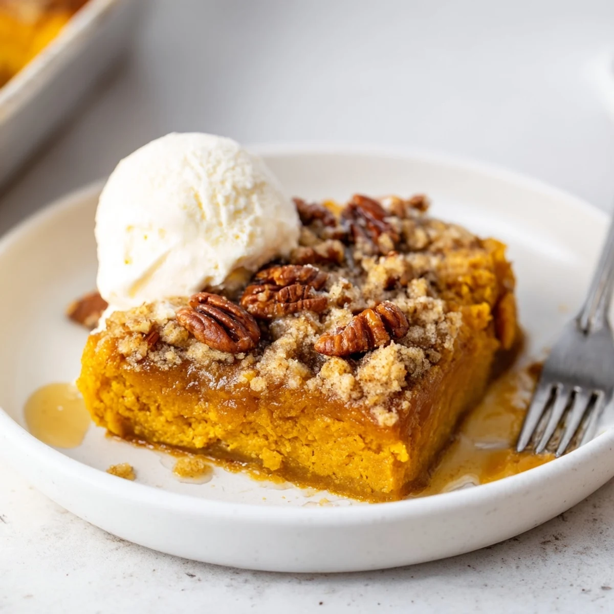 Slice of Pumpkin Dump Cake served with melting vanilla ice cream and fork