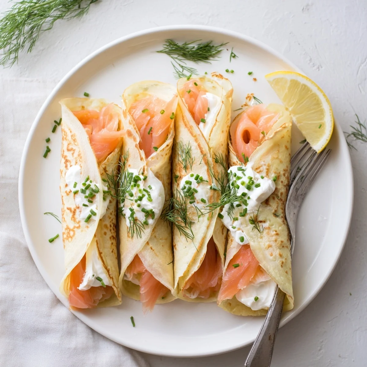 Elegant crepes filled with smoked salmon slices topped with chives and served with lemon wedges