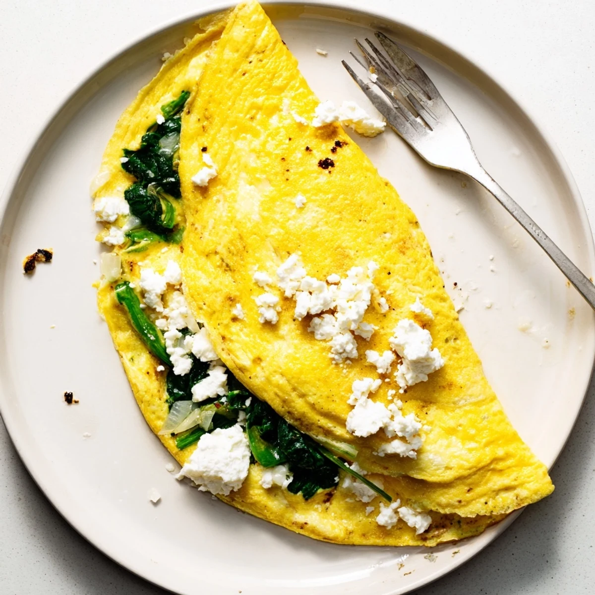 Golden spinach feta omelet recipe folded in half with white crumbled cheese