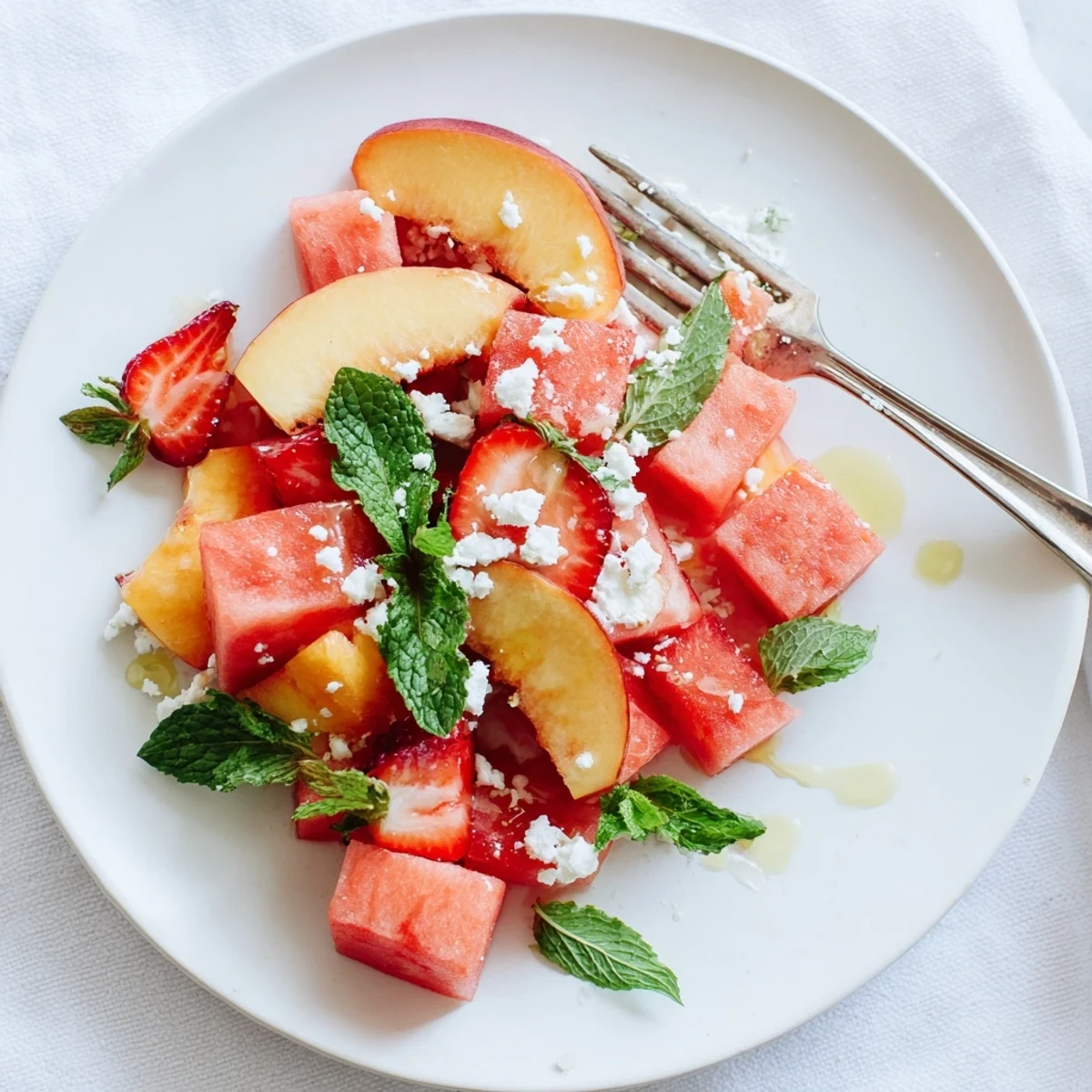 Fresh summer peach watermelon salad in a white bowl with mint leaves and lime drizzle