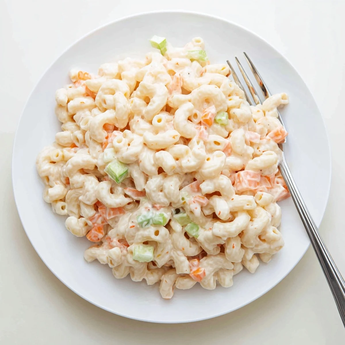 Creamy Hawaiian macaroni salad loaded with grated carrots and celery in a white serving bowl