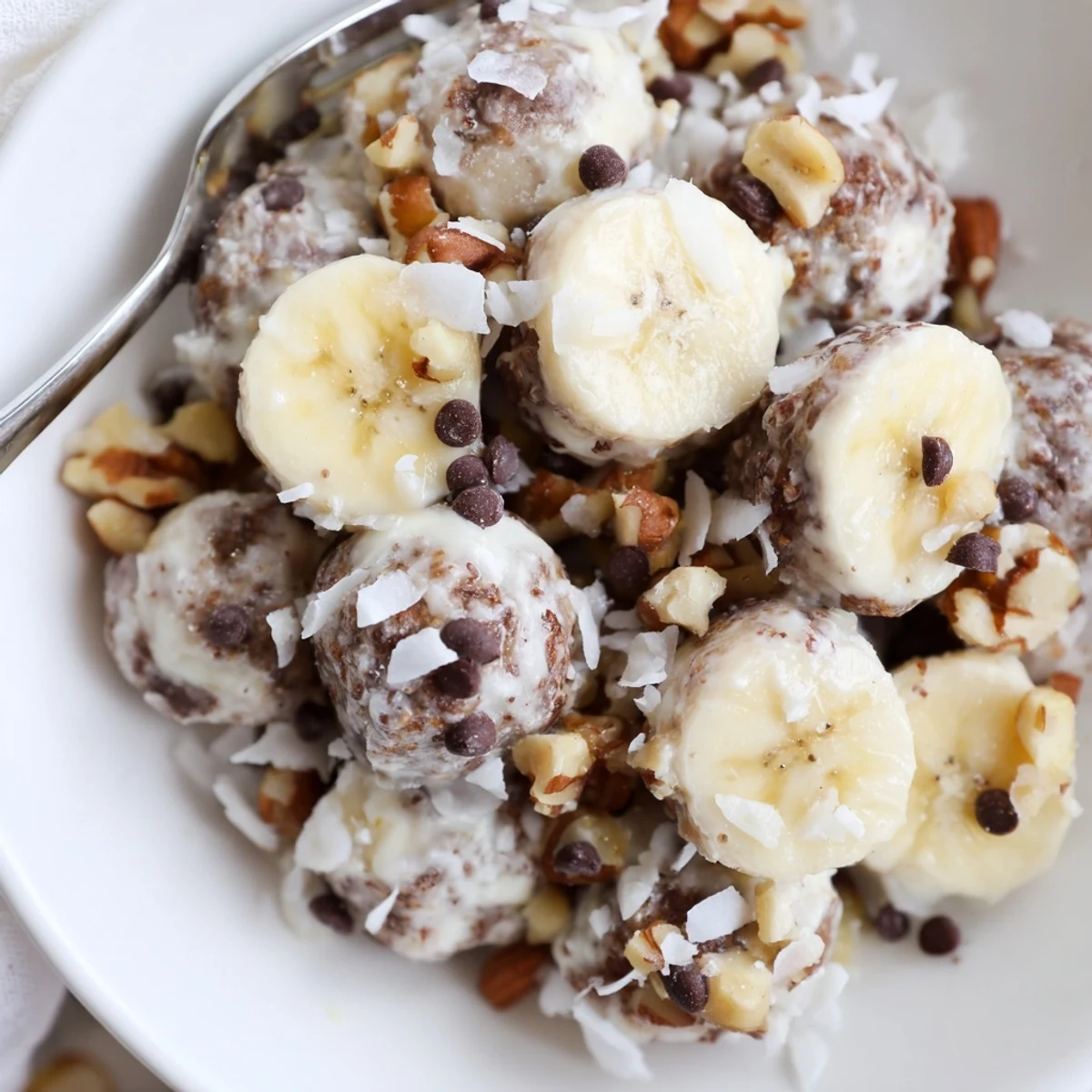 Hand holding Frozen Banana Yogurt Bites, creamy coating with toasted coconut flakes
