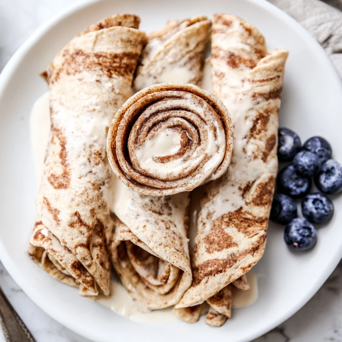 Warm Cinnamon Roll Protein Crepes Recipe rolled with creamy cinnamon filling, light glaze.