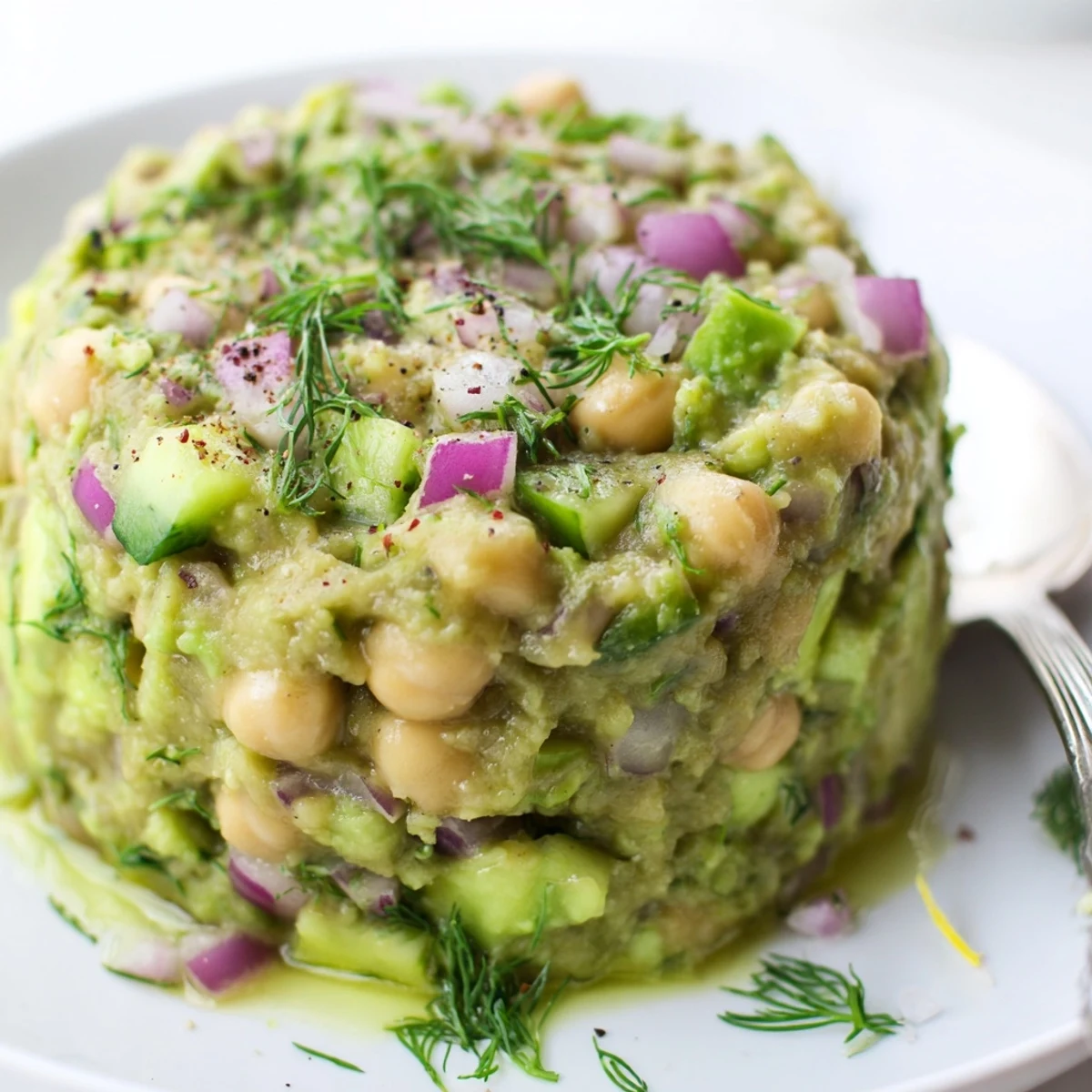 Chunky Smashed Chickpea Avocado Pickle in a bowl, dotted with red onion