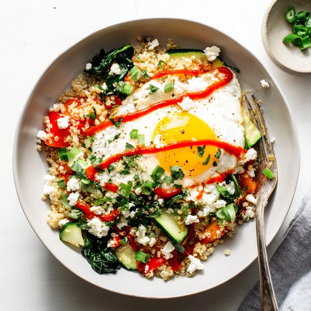 Colorful quinoa breakfast bowl featuring tender zucchini, a perfectly fried egg, and zesty sriracha