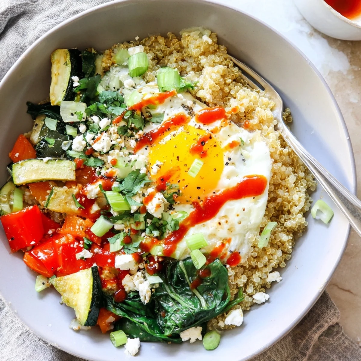 Warm savory quinoa breakfast bowl served with wilted spinach, fresh herbs, and golden yolk
