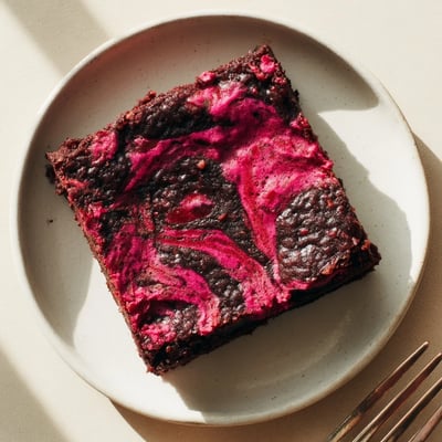 Freshly baked Raspberry Swirl Brownies with a crackly top, showcasing vibrant marbled puree and fudgy edges on a rustic wooden serving board.