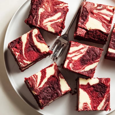A slice of Red Velvet Cheesecake Brownies on a white plate with a dollop of whipped cream, highlighting the fudgy red velvet base.