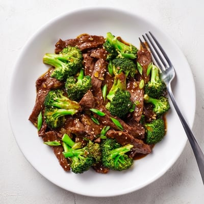 Close-up of Better Than Takeout Beef With Broccoli sizzling in a wok, featuring caramelized beef strips, bright green broccoli, and aromatic garlic and ginger.