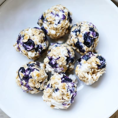 Blueberry Cheesecake Protein Bites on a white plate with a jar of honey nearby.