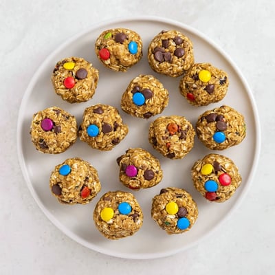 Perfectly portioned Monster Cookie Protein Balls sit on parchment, showcasing their no-bake texture with creamy peanut butter and candy-coated chocolate mix-ins.