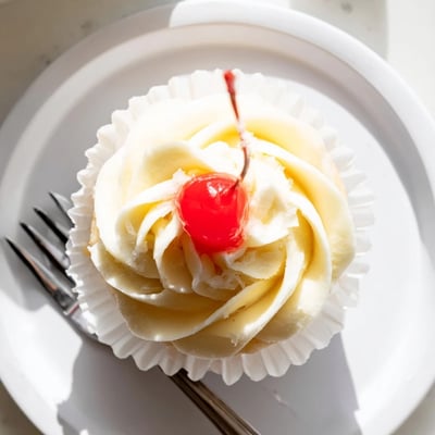 Fluffy pineapple frosting swirled on moist Dole Whip Cupcakes served on a pastel plate