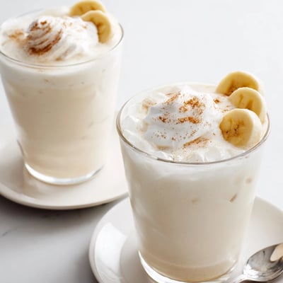 Tall Vanilla Banana Shake drizzled with maple syrup, banana slice garnish.